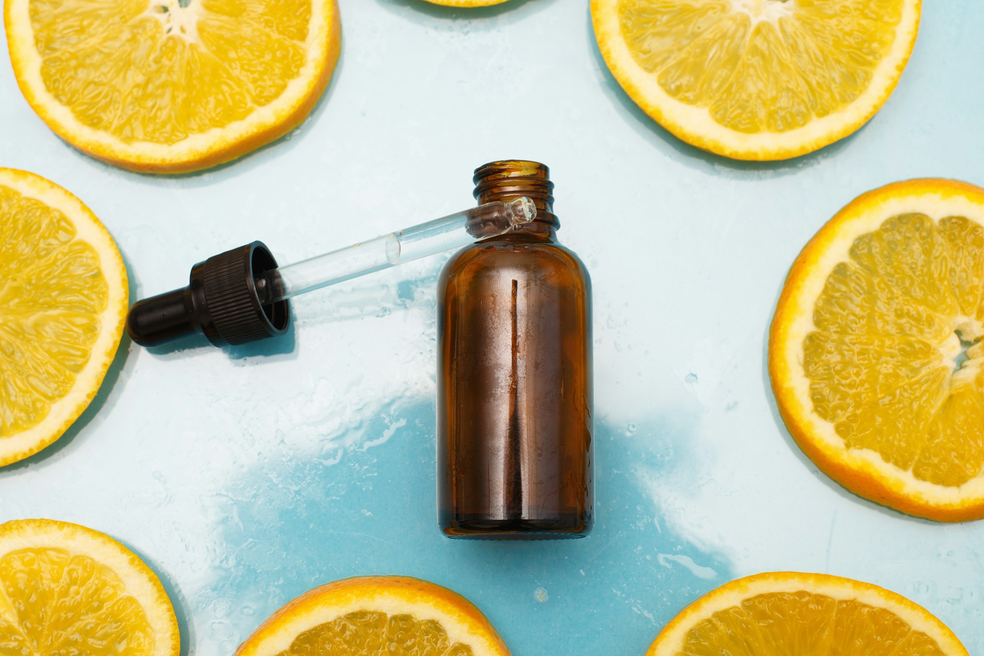 brown glass bottle with a pipette serum with vitamin C. Essential oil and orange slices.